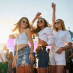 Three young women excited with hands in the air at an outdoor event in Destin.