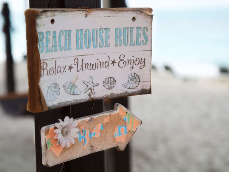 Sign on the beach that reads Beach House Rules: Relax, Unwind, Enjoy.