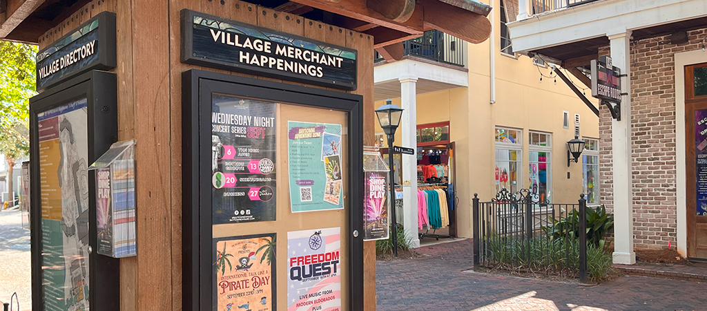 The Village of Baytowne Wharf entrance sign, with shops in the background.