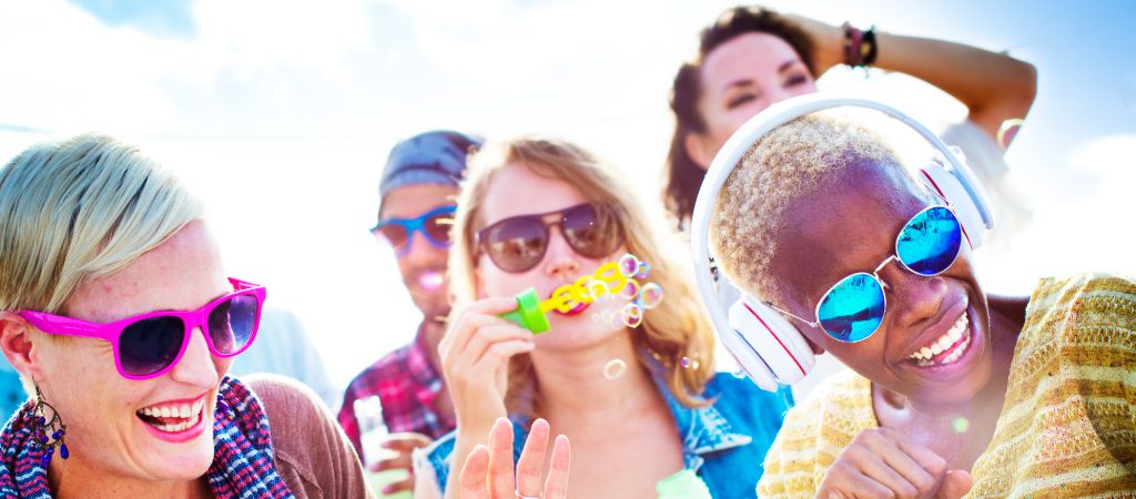 A group of women and a man laughing, dancing, and blowing bubbles on a sunny day in Panama City Beach.