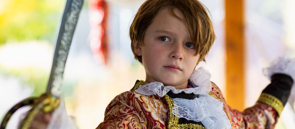 A young boy dressed as a pirate raises his sword in a fighting stance.