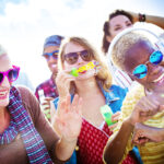 A group of women and a man laughing, dancing, and blowing bubbles on a sunny day in Panama City Beach.