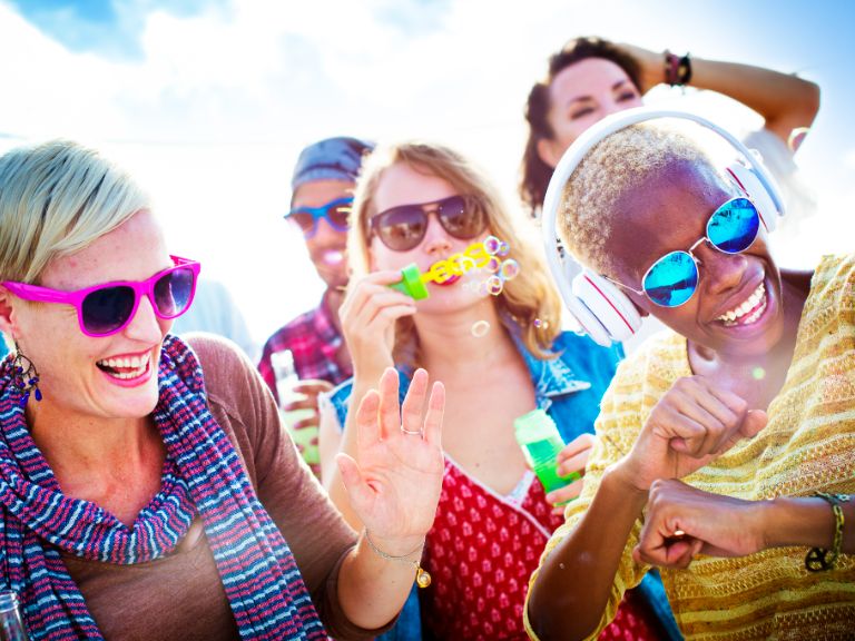 A group of women and a man laughing, dancing, and blowing bubbles on a sunny day in Panama City Beach.