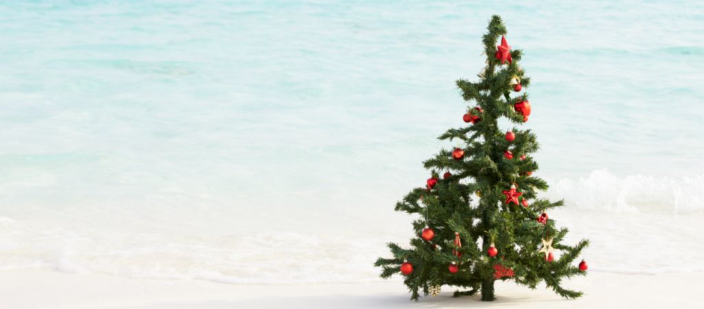 A small decorated Christmas tree sits on sugar-white sand, with Gulf Coast waves lapping in the background.