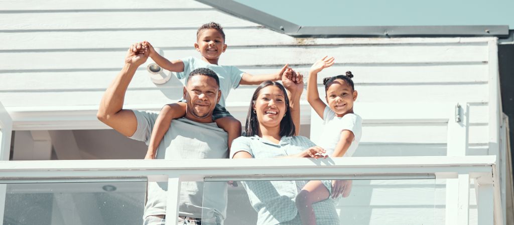 A young family smiles while standing on a beach house balcony.